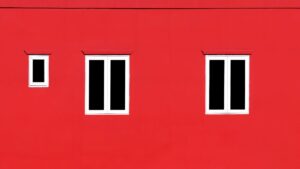 Close-up of a vibrant red wall featuring minimalist white windows.